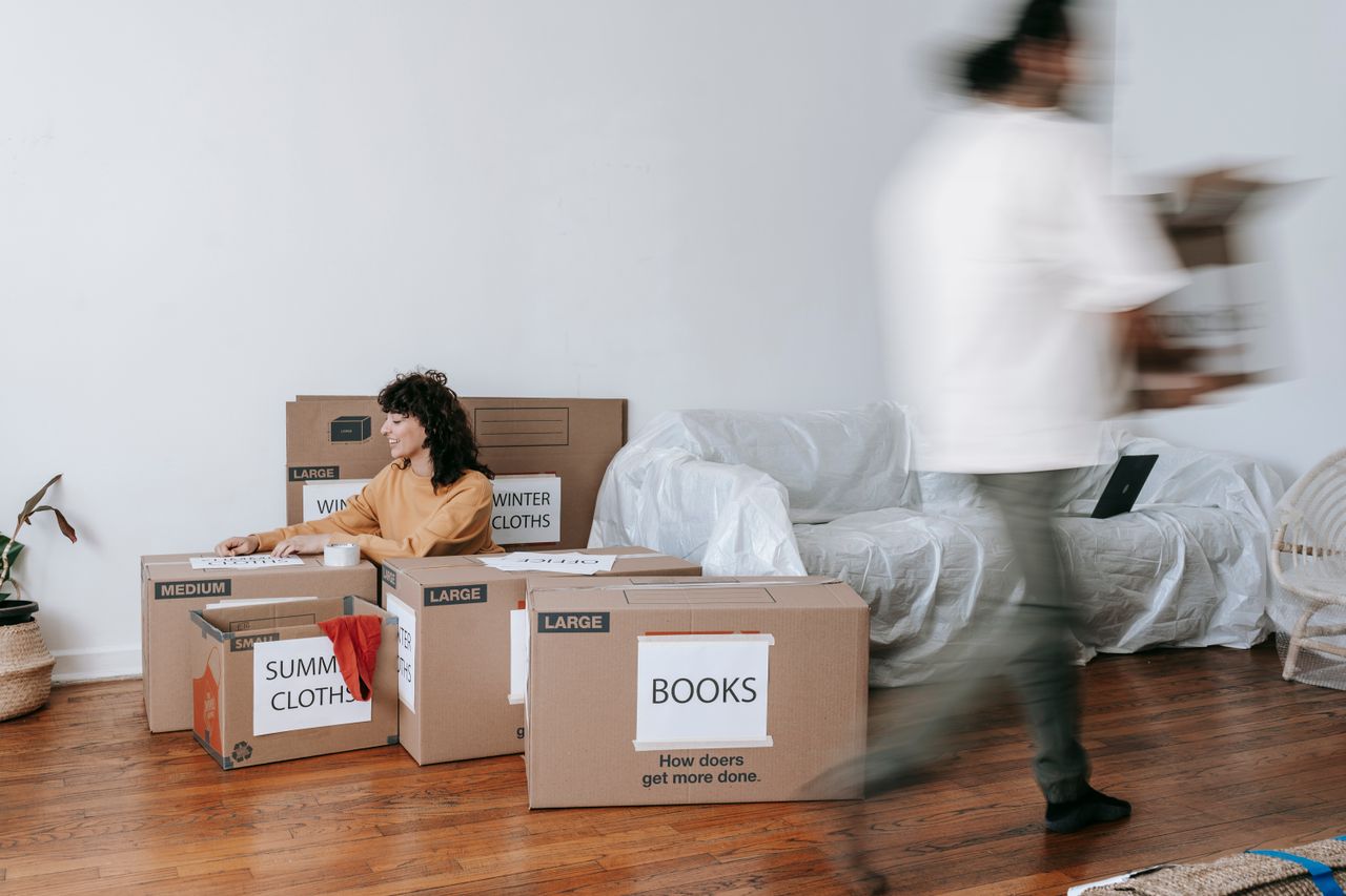 creative-03 A couple packing labeled boxes in a minimalist living room, preparing for moving day.