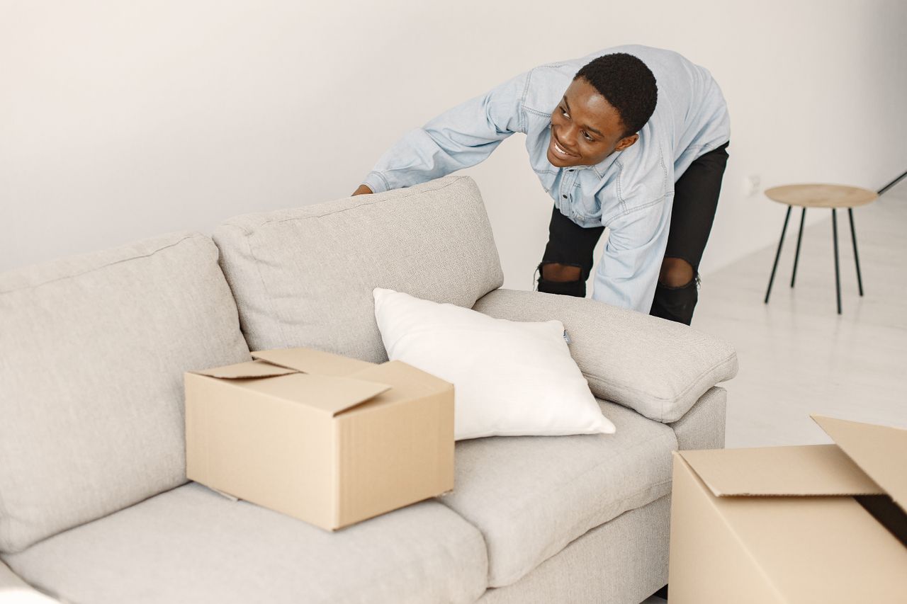 Services-01 Young man smiling while arranging cardboard boxes in a modern living room.